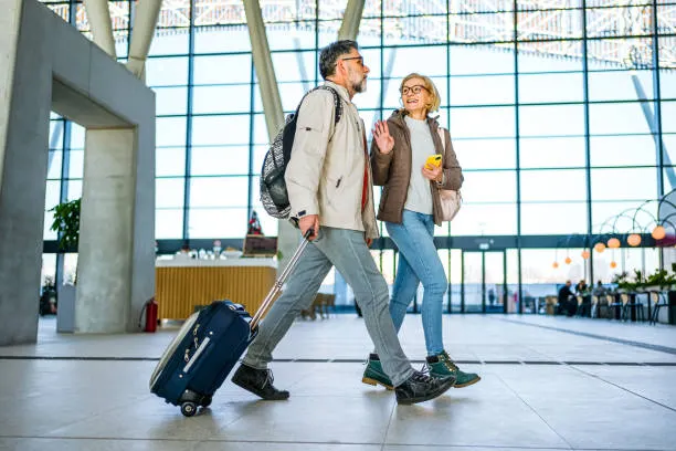 A mature couple walking through a bright train station with luggage while traveling